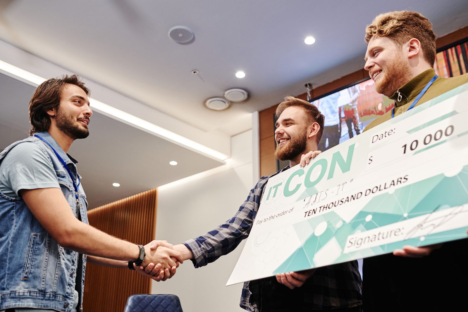 A smiling winner holding a giant award check while colleagues congratulate him