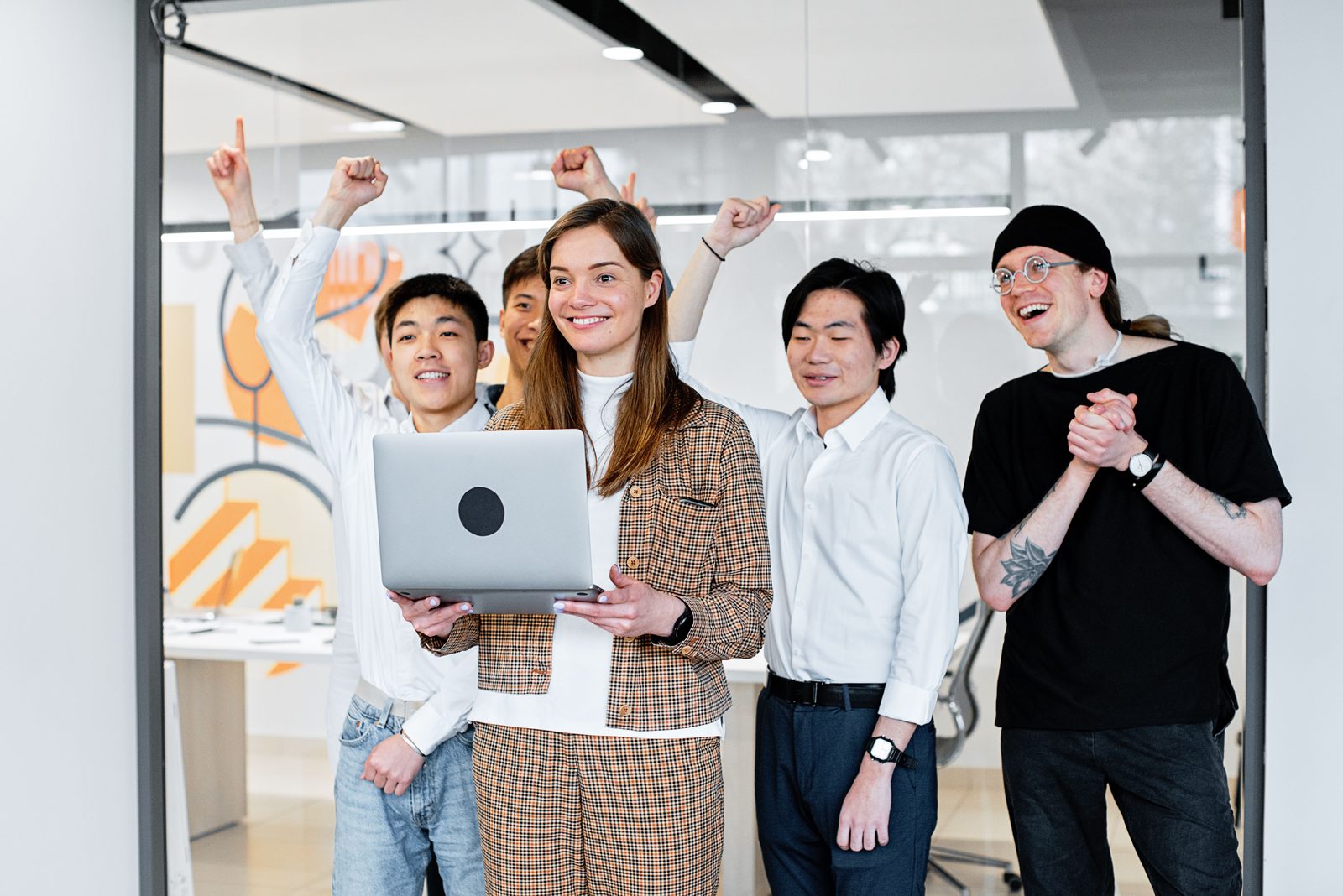 A startup team celebrating good news around a laptop in a modern office