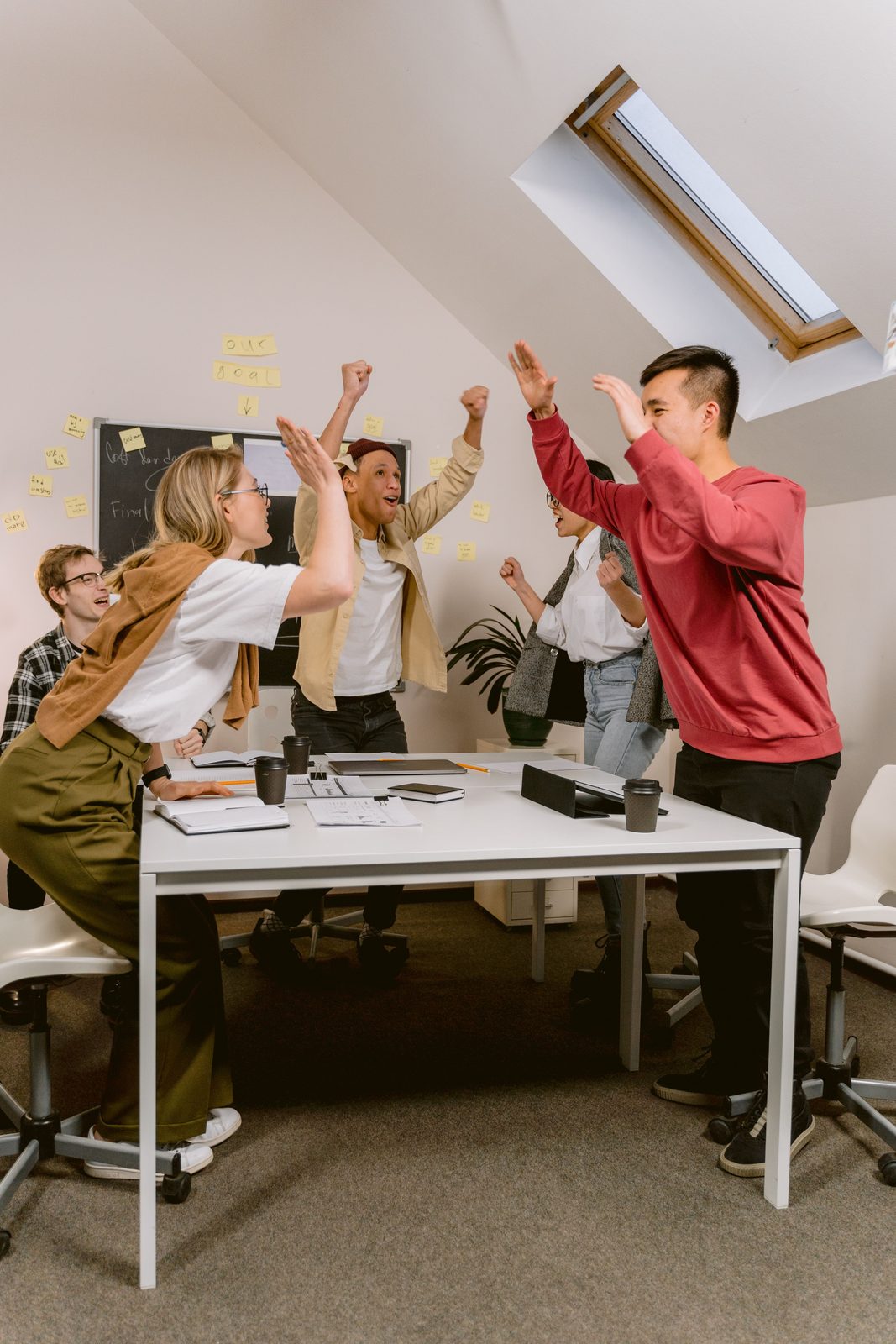A team celebrating around a meeting table with arms raised in front of a goal board